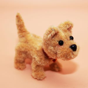 May include: A small, brown, furry toy dog with black eyes and a red collar. The dog is standing on a light pink surface.