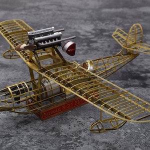 May include: A gold metal model of a Savoia S.21 flying boat with a detailed engine and propeller. The model is on a grey surface.