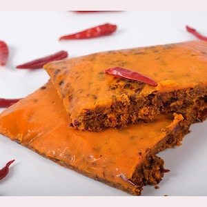 May include: Two pieces of orange-colored, spicy, dried meat with a flaky texture. The meat is topped with red chili flakes.