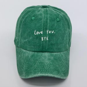 May include: A green baseball cap with the text "Love You, Bye" embroidered in white on the front.