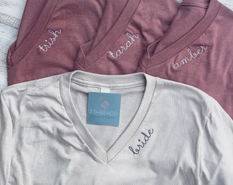 Puede incluir: Cuatro camisetas con nombres bordados. Tres son de color marrón con los nombres "Trish", "Tarah" y "Amber" bordados en blanco. La cuarta es beige con la palabra "bride" bordada en negro.