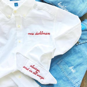 Könnte beinhalten: Ein weißes Hemd mit Knopfleiste, roter Stickerei "mrs dahlman" über der Tasche und "always, and in all ways" am Ärmelbündchen, über blauen Jeanshemden mit weiß gestickten Namen wie "madz", "kaitlyn" und "brit" platziert.