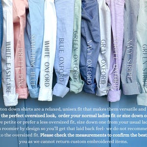 A collection of various button-down shirts in different colors and styles, including denim, white, blue, green, navy, and striped, hanging side by side.
