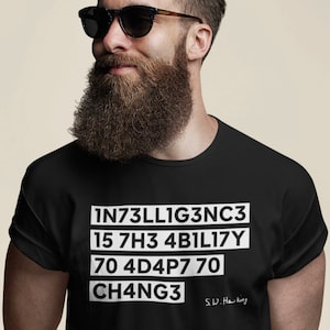 Puede incluir: Camiseta negra con texto blanco que dice "INT3LLIG3NC3 15 7H3 4B1L1TY 70 4D4P7 70 CH4NG3" y una firma que dice "S.W. Hawking".