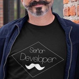 Könnte beinhalten: Ein schwarzes T-Shirt mit einer weißen rautenförmigen Grafik, auf der "Señor Developer" steht, darunter ein weißer Schnurrbart.