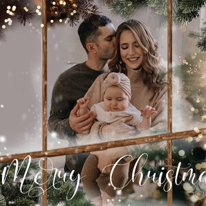 Peut inclure: Une famille de trois personnes pose pour une photo de Noël. Un homme et une femme tiennent un bébé vêtu d'une robe blanche et d'un turban rose. La famille est debout devant une fenêtre avec un fond enneigé. Le texte "Merry Christmas" est écrit en cursive blanche en bas de l'image.