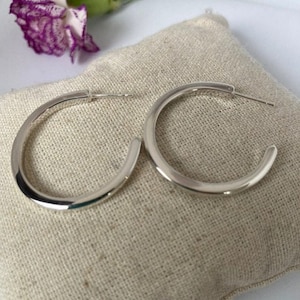 May include: A pair of silver hoop earrings. The hoops are thick and have a smooth, polished finish.