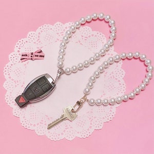 May include: A white pearl keychain with a silver car key and a silver key with the word "Sargent" on it.