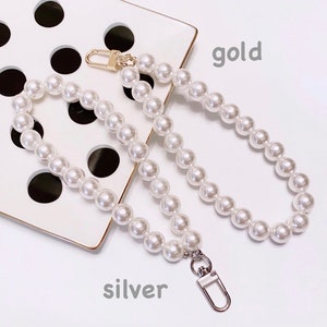 May include: A white pearl chain bag strap with gold and silver clasps. The strap is on a white surface with black polka dots. The words "gold" and "silver" are written below the strap.