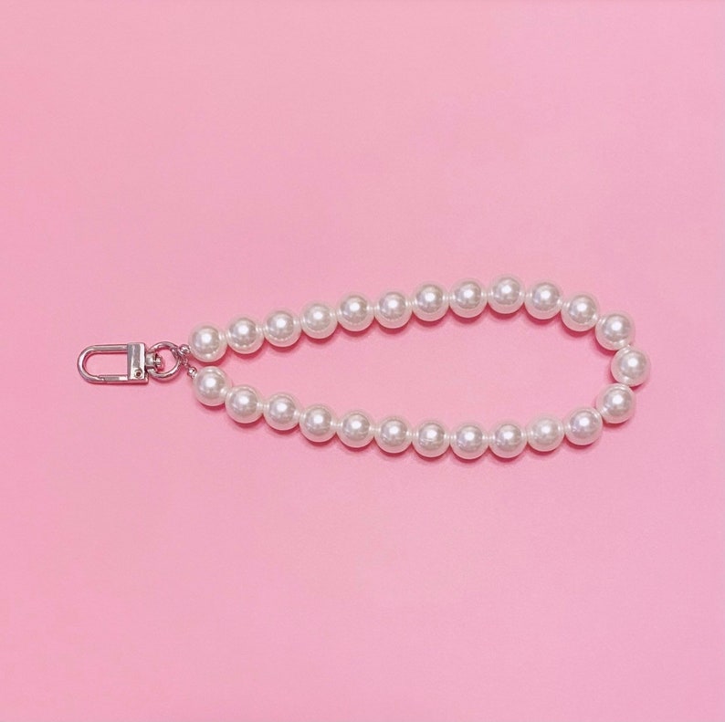 May include: A white pearl necklace with a silver clasp. The necklace is on a pink background.