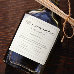 May include: A clear glass bottle with a white label that reads "The Lord of the Rings by The Cocktail Parlor Fangorn Forest". The label also includes a description of the scent, which is described as "Smells of eternal musk in a dank and charming tree-infested forest where journeys seek alternative paths moving both swiftly and slowly.  Fraser Fir, Oakmoss, Sangria, White Birch, Violet."