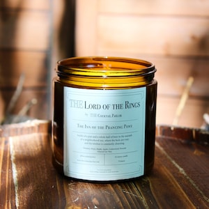 May include: A brown glass candle jar with a white label that reads "The Lord of the Rings by The Cocktail Parlor The Inn of the Prancing Pony". The label also includes a description of the candle scent and burn time.