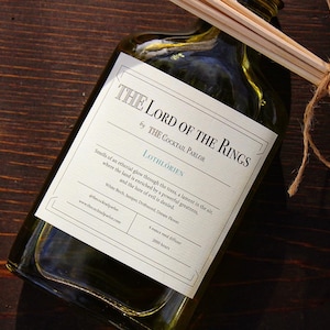 May include: A green glass reed diffuser with a label that reads "THE LORD OF THE RINGS" and "LOTHLORIEN." The diffuser includes wooden reeds tied with twine. The label also includes the text "THE COCKTAIL PARLOR."
