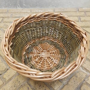 May include: A woven basket with a light brown exterior and a green and brown interior. The basket is made of natural materials and has a round shape.