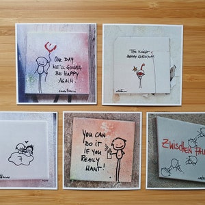 May include: Five square tiles with hand-drawn illustrations and inspirational messages. The tiles feature a red heart balloon, a knight, a couple on a cloud, a person spraying paint, and a group of people falling. The messages on the tiles are "One day we'll gonna be happy again", "The knight before christmas", "You can do it if you really want!" and "Zwischen fall".