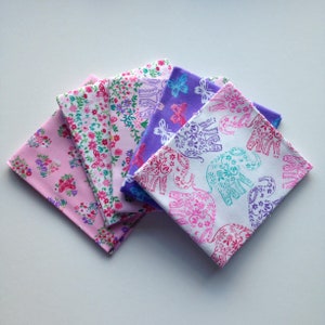 May include: A stack of five fabric squares with different patterns. The top square has a white background with pink and teal elephants. The second square has a purple background with white butterflies. The third and fourth squares have a pink background with white flowers and butterflies. The bottom square has a pink background with white flowers and butterflies.