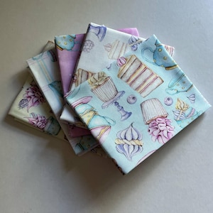 May include: Several folded fabric squares with pastel patterns. The designs feature cupcakes, teacups, cakes, and berries. The fabrics are in shades of blue, pink, purple, and yellow, creating a whimsical, dessert-themed aesthetic.