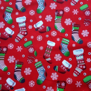 May include: Red fabric with a repeating pattern of white snowflakes and colourful Christmas stockings. The stockings are decorated with different patterns and colours.