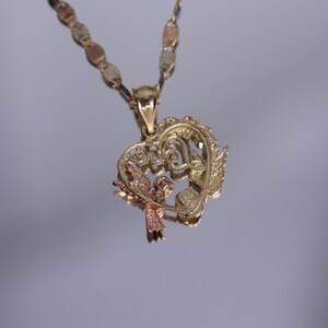 May include: A gold heart-shaped pendant necklace with a delicate design featuring a bird and the word "Love". The chain is made of three-toned gold.