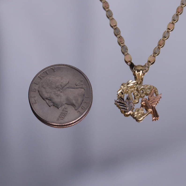 May include: A gold, silver, and rose gold necklace with a heart-shaped pendant featuring two hummingbirds and floral accents. The pendant is about the size of a US quarter.