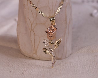May include: A gold rose pendant necklace with a two-tone design. The rose is made of yellow and rose gold and has a delicate stem and leaves.