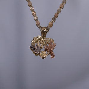May include: A gold heart-shaped pendant necklace with two birds, one in gold and one in rose gold, perched on a branch with leaves. The chain is a gold, diamond-cut, rope chain.