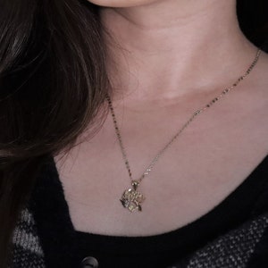 May include: A gold chain necklace with a delicate, intricate pendant hangs on a person's neck. The necklace is worn against a black shirt with a plaid pattern.
