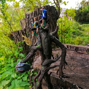May include: A tree-like figure with a rough, brown bark texture, standing on a wooden surface. Three small figures are perched on the tree, two wearing blue and green clothing and one wearing a green and brown outfit.