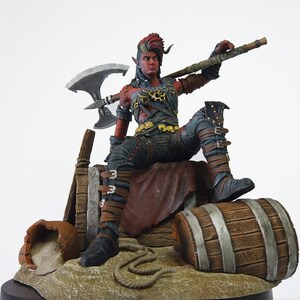 May include: A detailed figurine of a red-skinned humanoid with horns, wearing black and gold armor, and holding a large axe. The figure is seated, with one leg resting on a wooden barrel. The base includes a broken pot and rope.