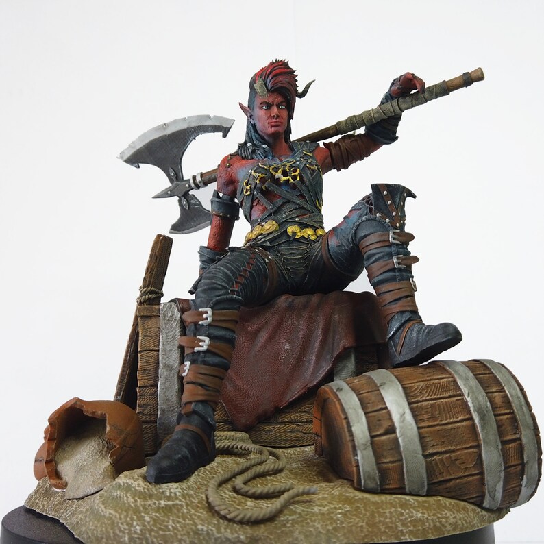 May include: A detailed figurine of a red-skinned humanoid with horns, wearing black and gold armor, and holding a large axe. The figure is seated, with one leg resting on a wooden barrel. The base includes a broken pot and rope.