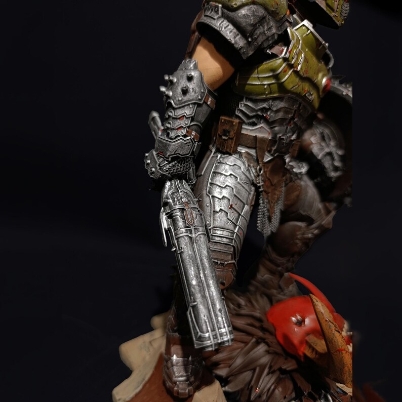 May include: A detailed action figure of a demon warrior with green and silver armour, holding a large gun. The figure is standing on a base with a skull and other details.
