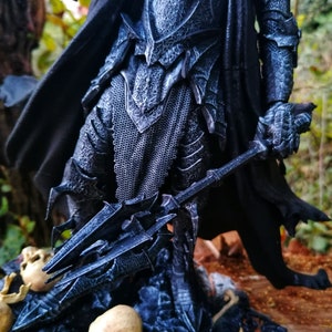 Op de afbeelding: Een donkergrijze en zwarte action figure van een krijger die een harnas draagt en een wapen met punten vasthoudt. De figuur staat op een basis met schedels en botten.