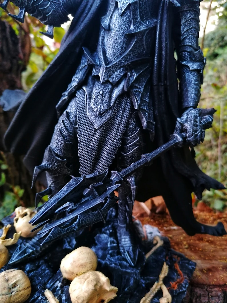 Op de afbeelding: Een donkergrijze en zwarte action figure van een krijger die een harnas draagt en een wapen met punten vasthoudt. De figuur staat op een basis met schedels en botten.