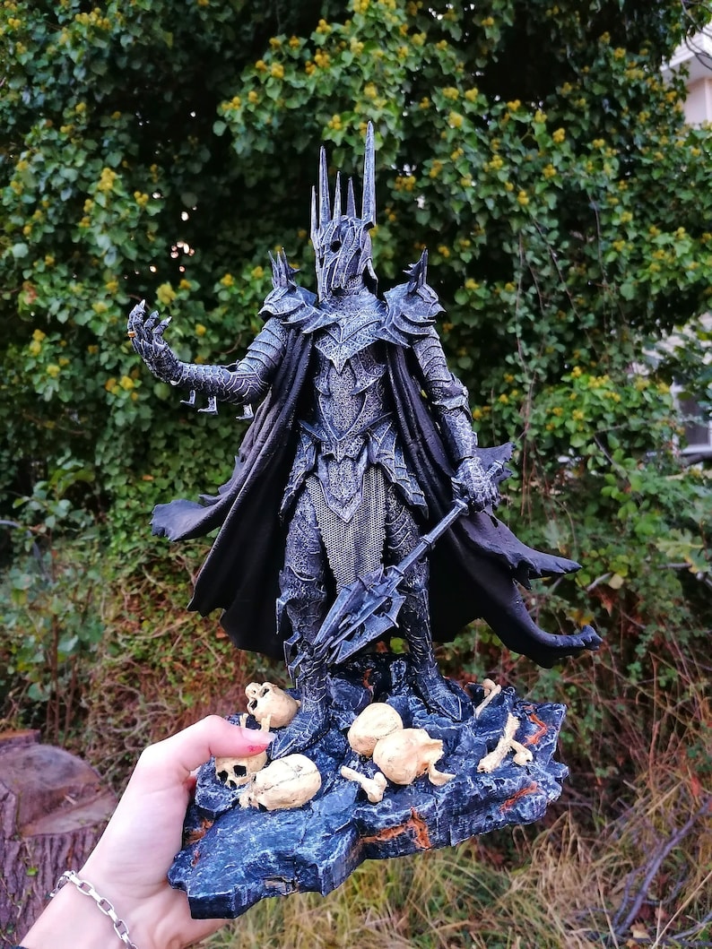 Op de afbeelding: Een zwart en zilveren beeld van het Lord of the Rings-personage, de Heksenkoning van Angmar, staand op een basis met schedels en botten. Het beeld houdt een zwaard in zijn rechterhand.