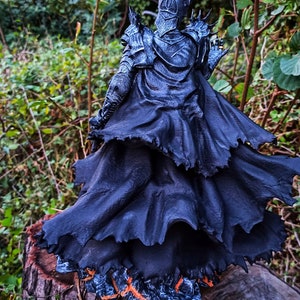 Op de afbeelding: Een zwart en zilveren beeldje van een duistere heer met een kroon en een vloeiende zwarte cape. Het beeldje staat op een boomstronk.
