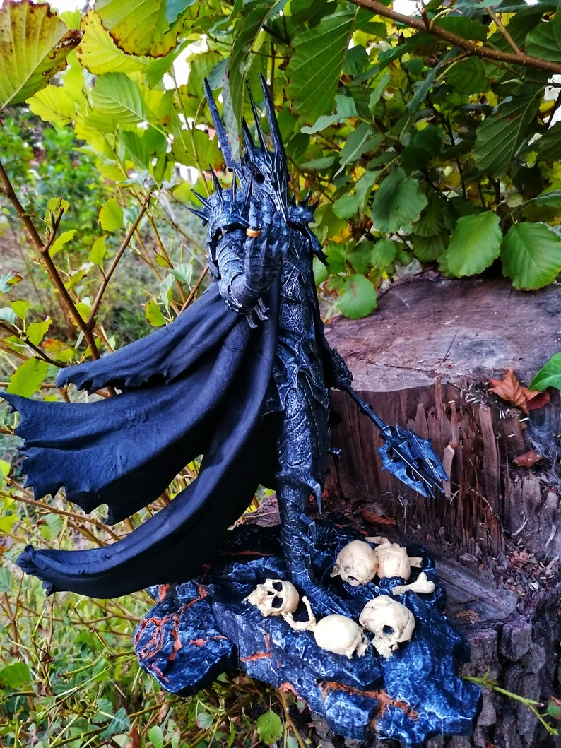 Op de afbeelding: Een zwart en zilveren beeldje van een duistere heer met een kroon en een cape, staand op een basis met schedels. Het beeldje is geposeerd met een hand omhoog, een ring vasthoudend.