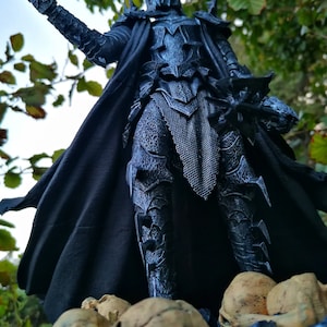Op de afbeelding: Een zwart en zilveren action figure van een duistere heer die een kroon en harnas draagt, een zwaard vasthoudt en op een basis met schedels staat.