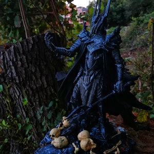 Op de afbeelding: Een donker, gedetailleerd beeldje van het Lord of the Rings-personage, de Heksenkoning van Angmar, staand op een basis met schedels en botten. Het beeldje is gemaakt van zwart plastic en heeft een dreigende uitdrukking.