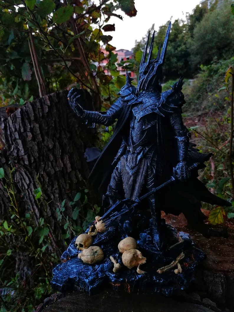 Op de afbeelding: Een donker, gedetailleerd beeldje van het Lord of the Rings-personage, de Heksenkoning van Angmar, staand op een basis met schedels en botten. Het beeldje is gemaakt van zwart plastic en heeft een dreigende uitdrukking.