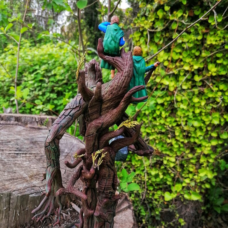 May include: Two figures in green and blue clothing stand on a tree trunk with a gnarled, brown, and textured surface. The figures are standing on a branch that extends out from the trunk. The background is a green leafy bush.