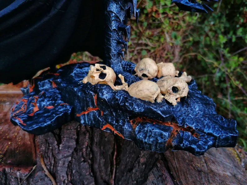 Op de afbeelding: Een zwarte en blauwe rotsbasis met een verzameling kleine, witte schedels. De basis is getextureerd en heeft een ruw, onregelmatig oppervlak.