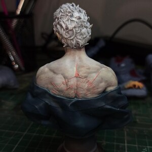 Op de afbeelding: Een geschilderd buste van een persoon met kort, wit haar. De buste is van de camera afgekeerd, waardoor de achterkant van de figuur zichtbaar is. De figuur heeft een gedetailleerd, gebeeldhouwd rug met rode markeringen.