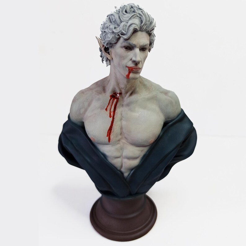Op de afbeelding: Een bustebeeld van een bleke, mannelijke figuur met puntige oren, die een donkerblauwe robe draagt. De figuur heeft bloed dat van zijn mond en borst druppelt.