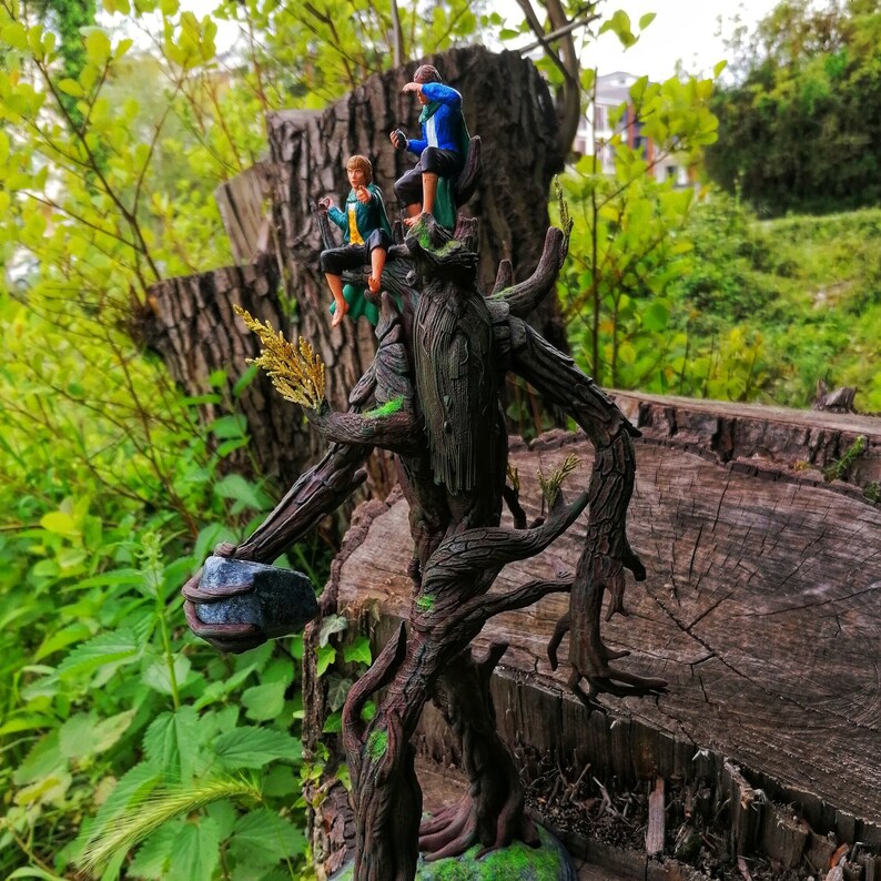 May include: A tree-like figure with a rough, brown bark texture, standing on a wooden surface. Three small figures are perched on the tree, two wearing blue and green clothing and one wearing a green and brown outfit.