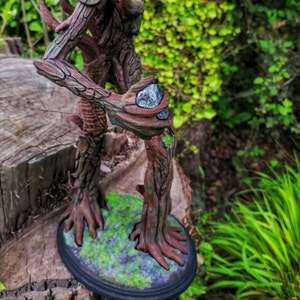 May include: A tree-like figure with brown bark and green moss, standing on a round base. The figure is holding a gray stone in its hand.