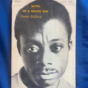 Könnte beinhalten: Ein Taschenbuch mit dem Titel Notes of a Native Son von James Baldwin. Das Cover zeigt ein schwarz-weißes Porträt einer Person mit kurzem, dunklem Haar. Der Text Beacon, BP 39 und $1.45 ist oben auf einem cremefarbenen Hintergrund gedruckt.