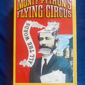 May include: A rectangular book cover titled The Complete Monty Python's Flying Circus with a yellow border and red background. It features a collage of a man in a suit with a typewriter on his head and a keyboard in his mouth, with text reading ALL THE WORDS.