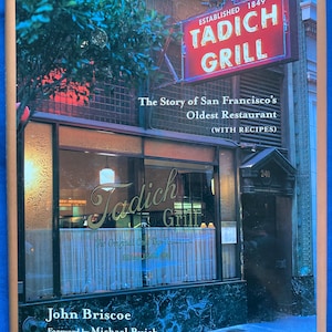 Könnte beinhalten: Ein gebundenes Buch mit dem Titel Tadich Grill: The Story of San Francisco's Oldest Restaurant (WITH RECIPES) von John Briscoe. Das Cover zeigt ein Foto des Restaurant-Außenbereichs mit einem roten Neonschild und dem Text Established 1849.