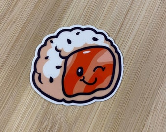 May include: A cartoon sushi roll with a smiling face and a winking eye. The sushi is pink and white with black sesame seeds on top. The sushi roll is on a wooden background.