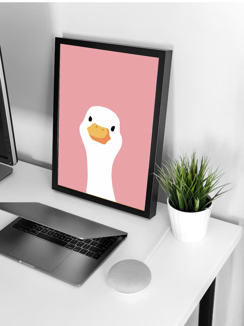 Puede incluir: Una impresi&oacute;n enmarcada de un ganso blanco con un pico naranja sobre un fondo rosa.